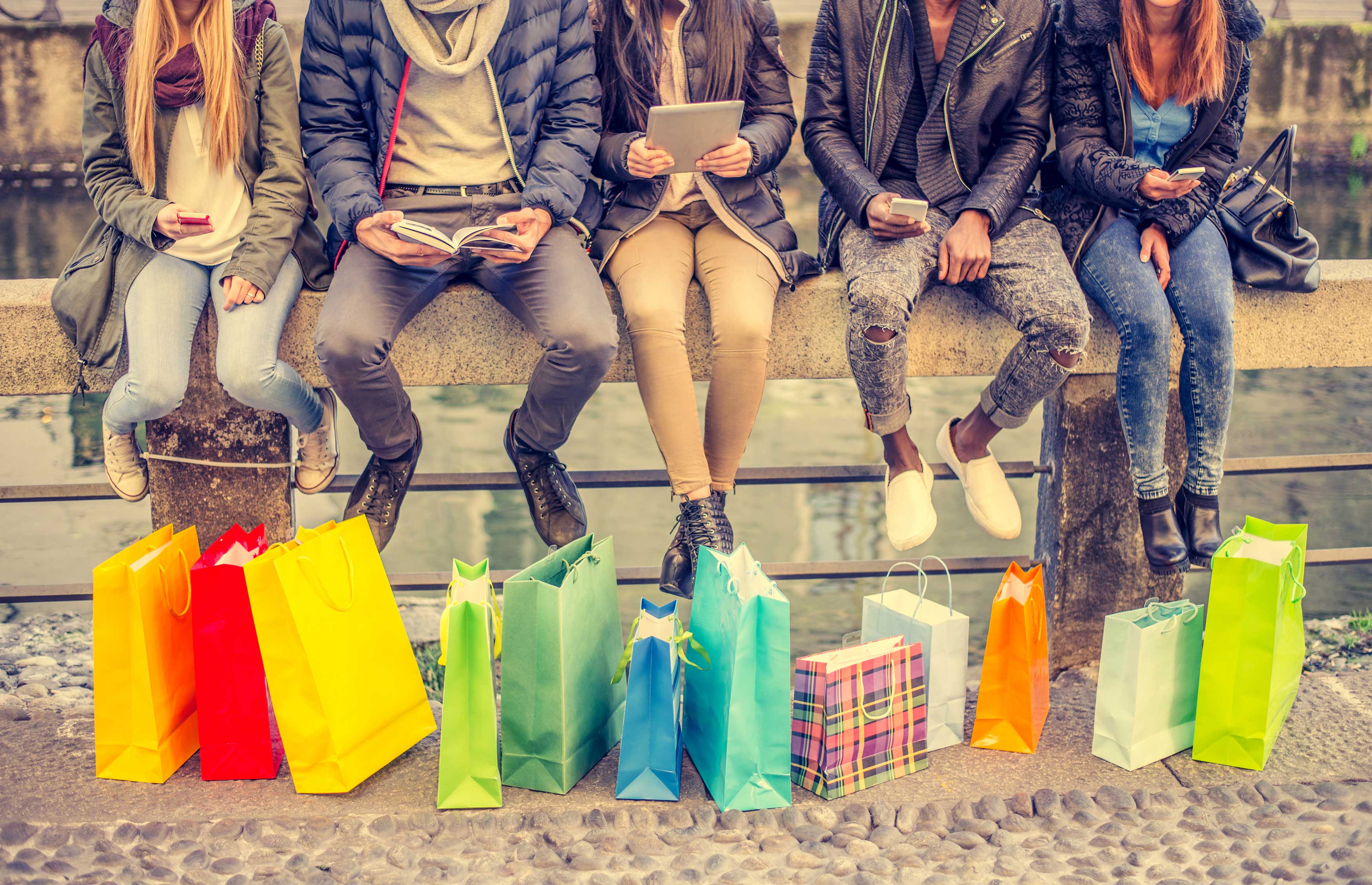 Group of 5 people sitting on a wall with many coloured shopping bags at their feet