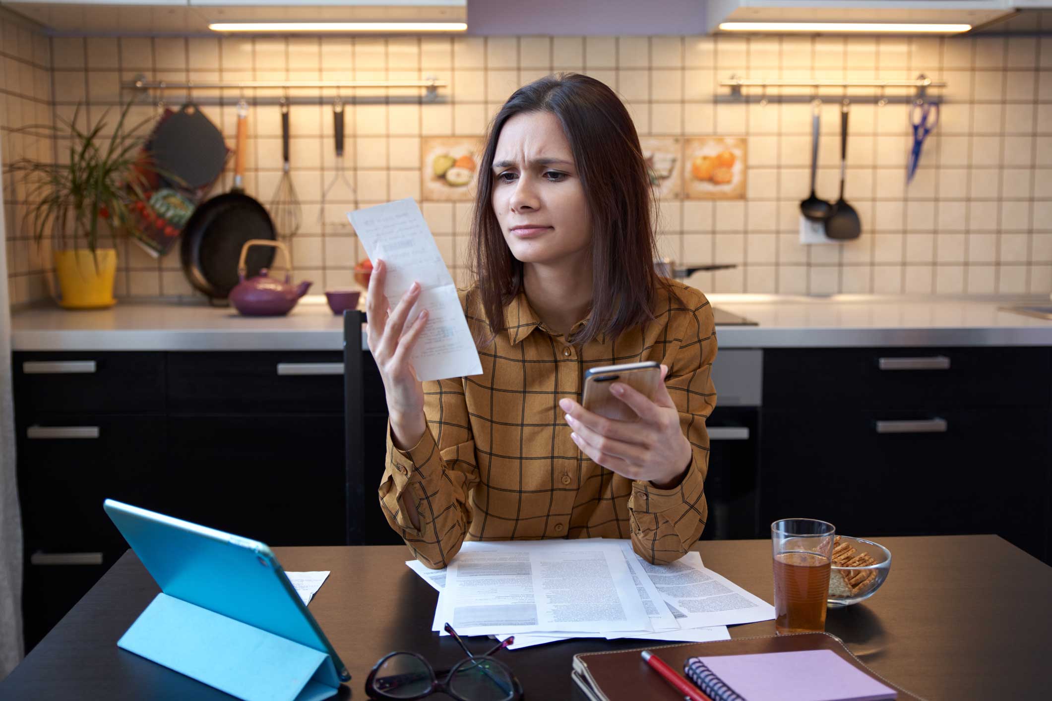 A woman in her kitchen examining a receipt in her hand