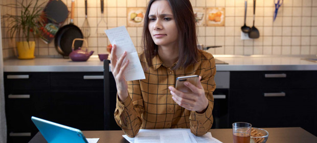 A woman in her kitchen examining a receipt in her hand