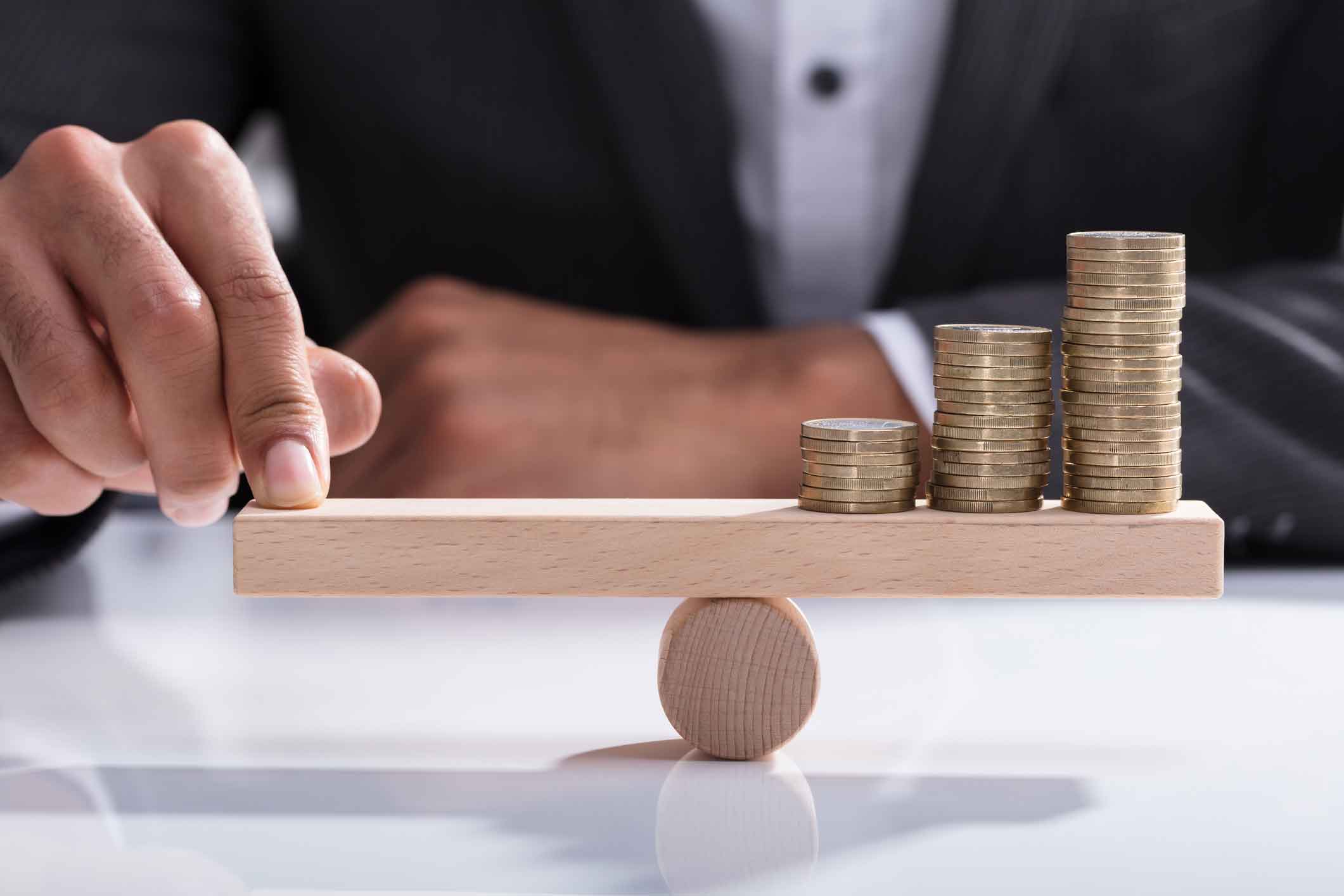 A man in a suit balancing coins on a wooden b#LOCK balancing scales