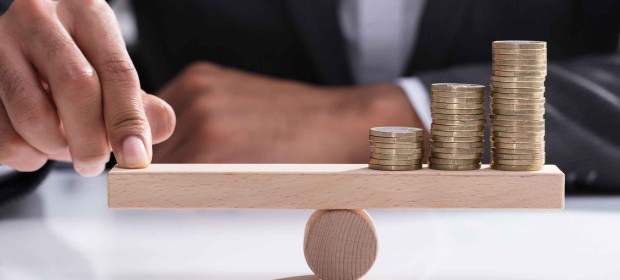 A man in a suit balancing coins on a wooden b#LOCK balancing scales