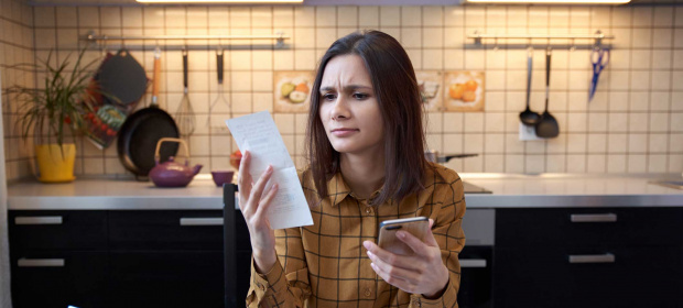 A woman in her kitchen examining a receipt in her hand