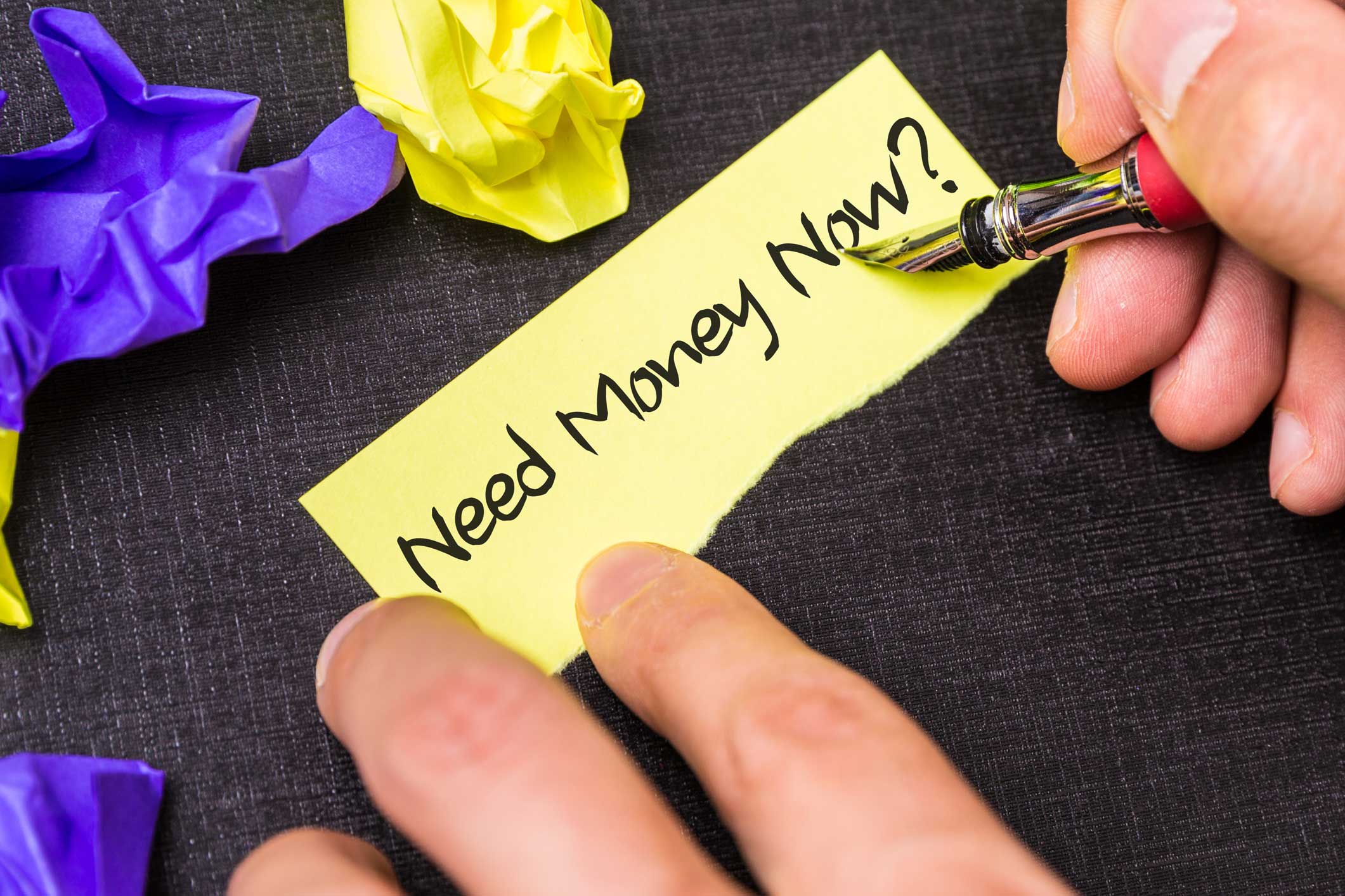 Someone writing need money now on a torn post-it note