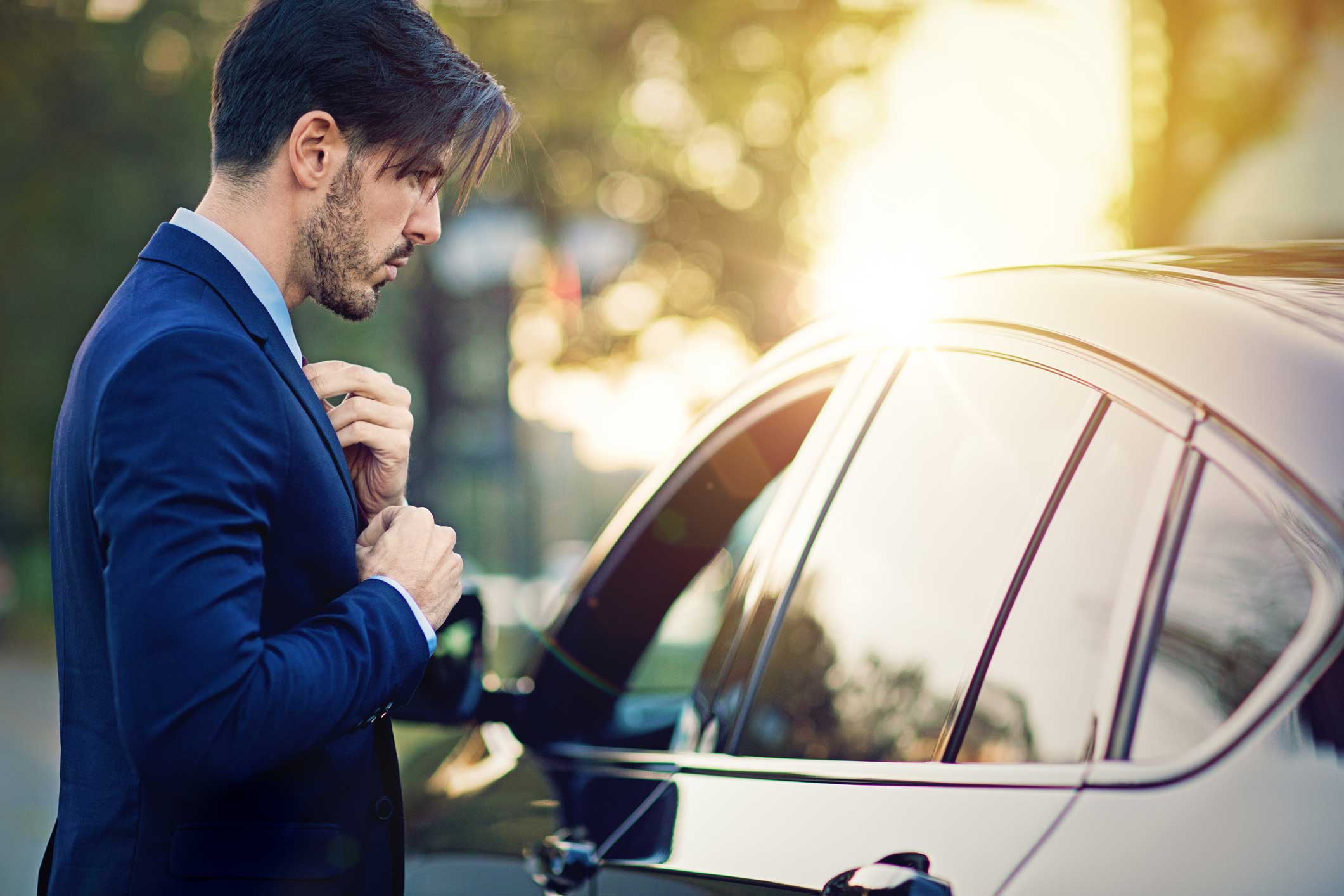 A man fixing his suit tie in a car window reflection