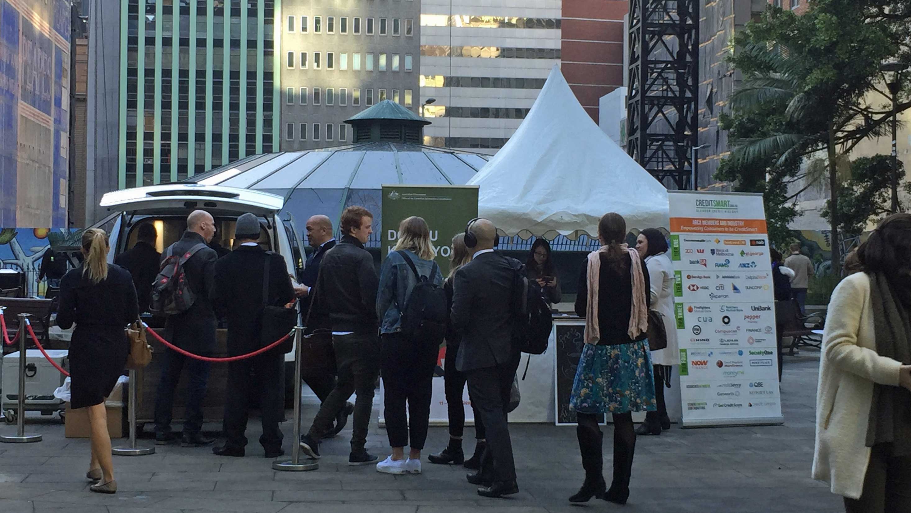 A group of people queing at a CreditSmart stand outside