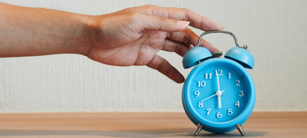 A hand reaching out to a blue alarm clock