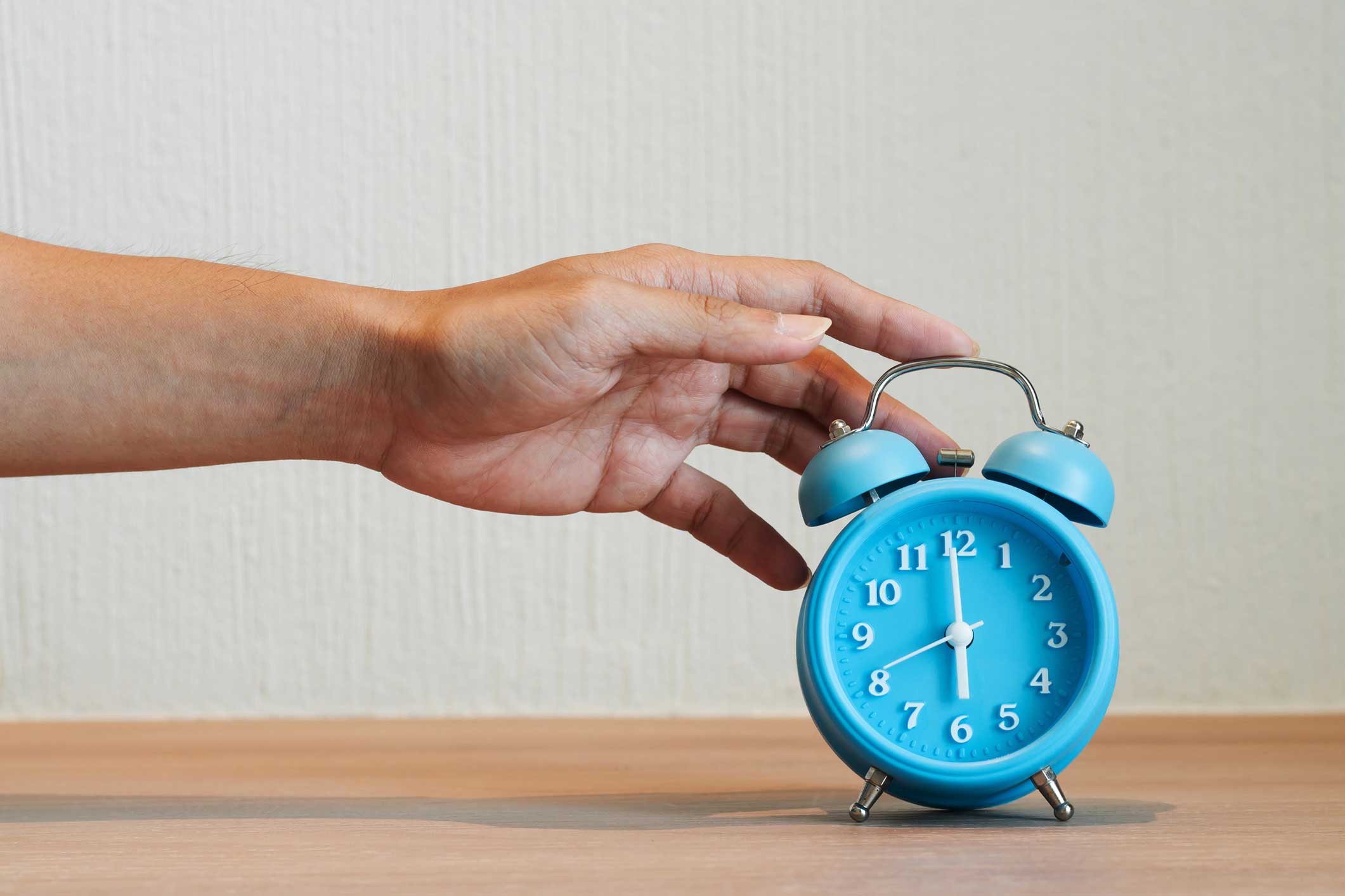 A hand reaching out to a blue alarm clock